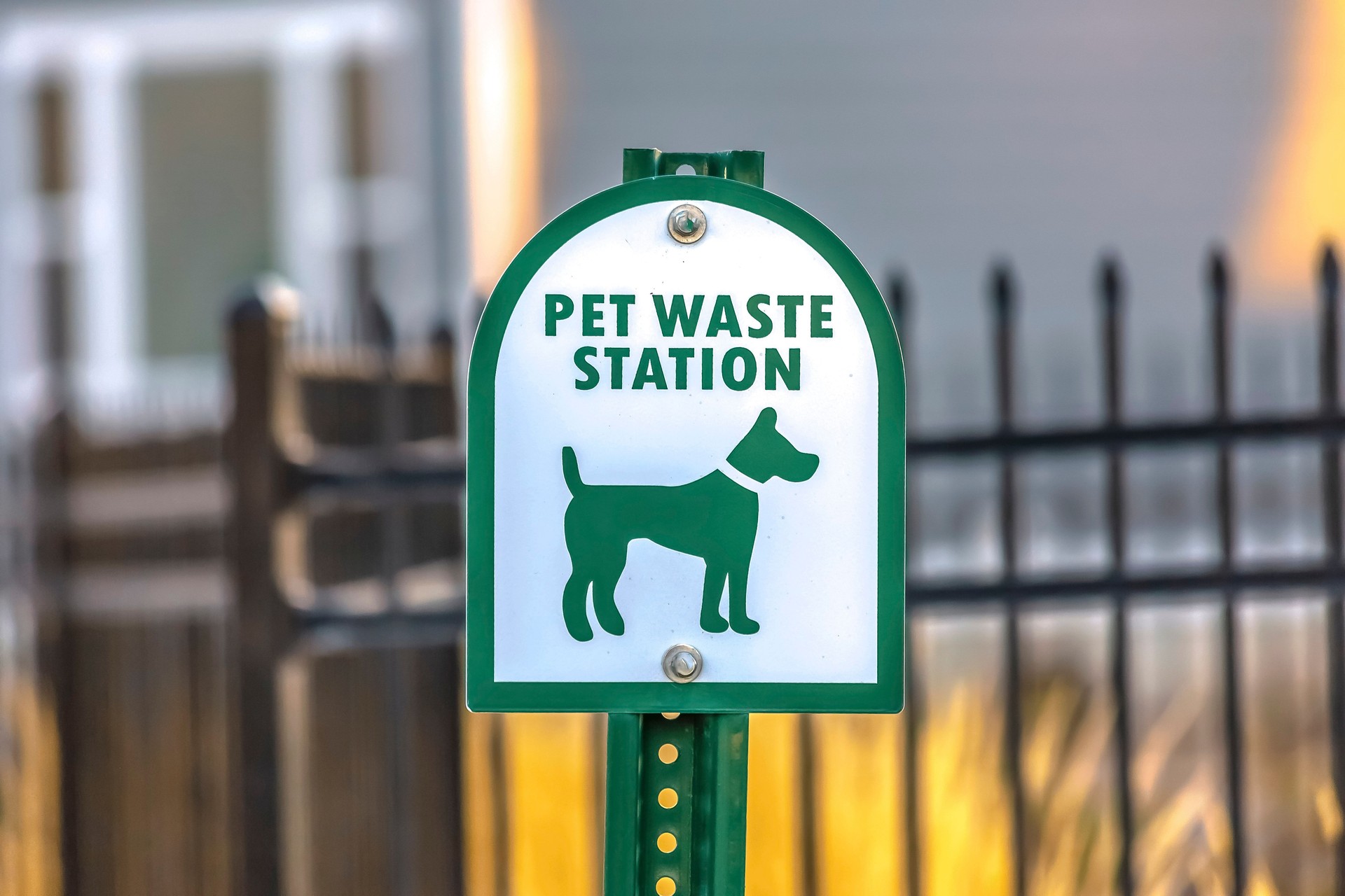 Close up of a Pet Waste Station with gate and building in the blurry background